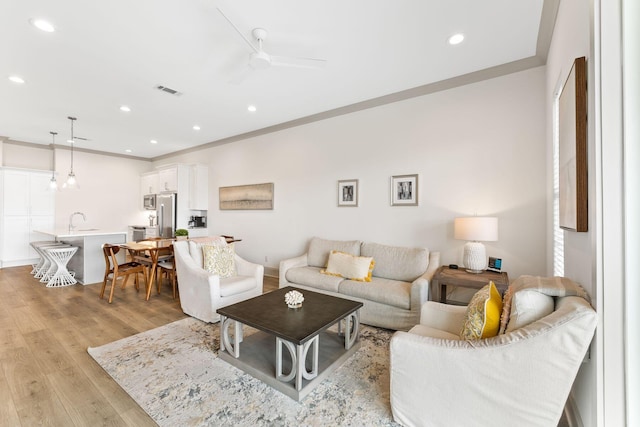 living room featuring light wood-type flooring, ceiling fan, crown molding, and sink