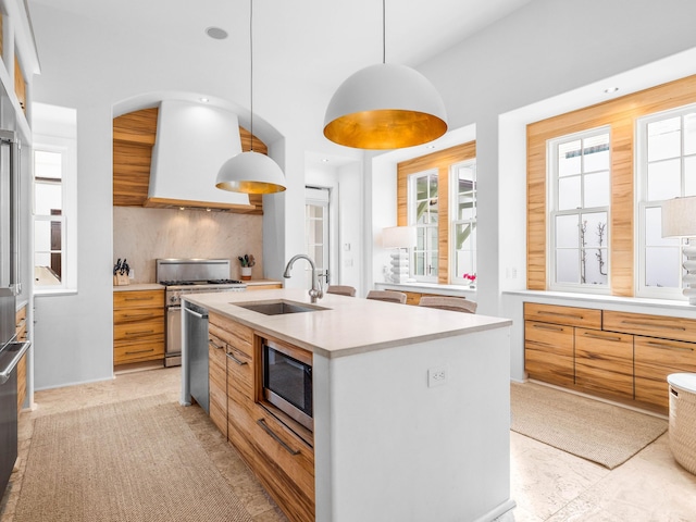 kitchen with pendant lighting, an island with sink, sink, exhaust hood, and stainless steel appliances