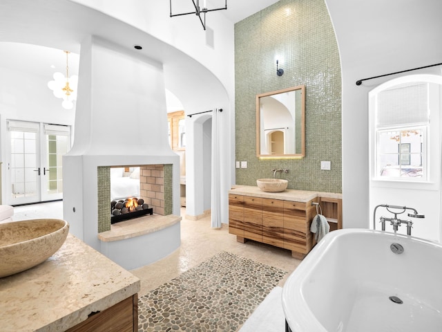 bathroom featuring a multi sided fireplace, vanity, a notable chandelier, a towering ceiling, and a washtub