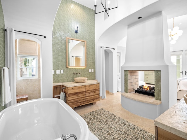 bathroom with a multi sided fireplace, a bath, a high ceiling, and a notable chandelier