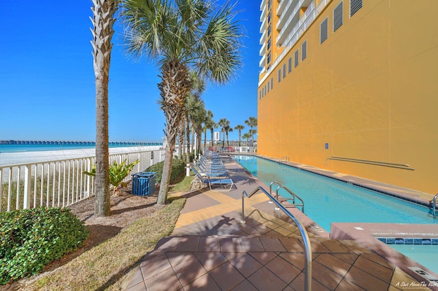 view of pool featuring a patio area, a water view, and a beach view