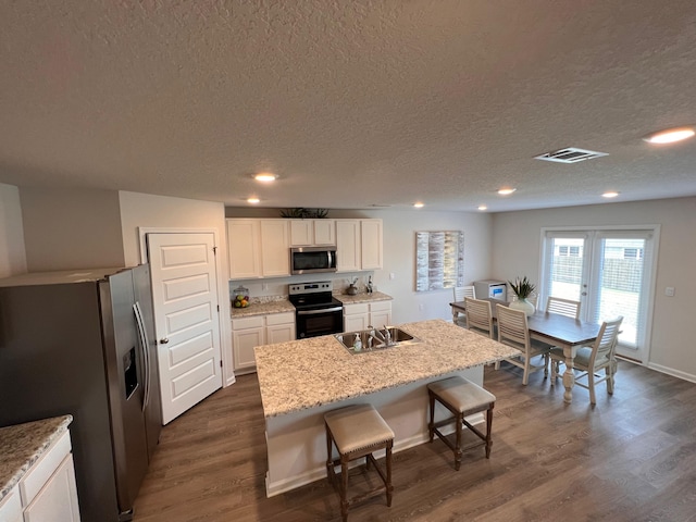 kitchen with dark wood-type flooring, white cabinets, an island with sink, appliances with stainless steel finishes, and a kitchen bar