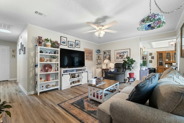 living room featuring wood-type flooring, a textured ceiling, ceiling fan, and ornamental molding