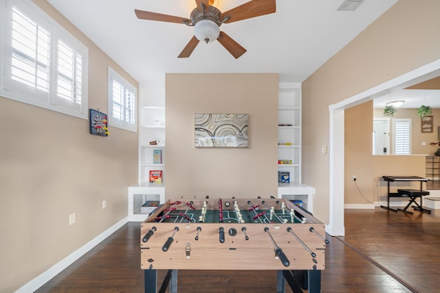 game room featuring built in shelves, a wealth of natural light, ceiling fan, and dark wood-type flooring