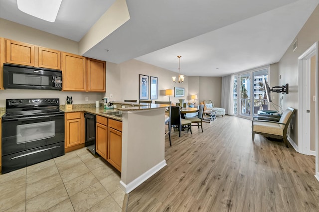 kitchen featuring stone counters, a notable chandelier, kitchen peninsula, black appliances, and light wood-type flooring