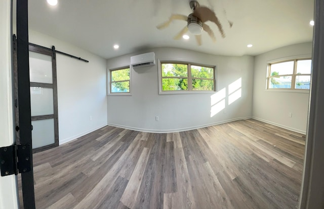 unfurnished room with wood-type flooring, a barn door, a wall unit AC, and ceiling fan