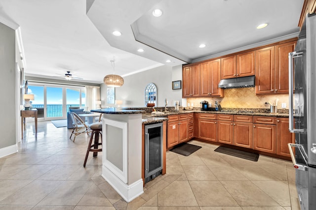 kitchen with a kitchen breakfast bar, dark stone countertops, kitchen peninsula, and beverage cooler