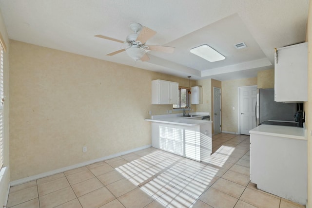 kitchen with a tray ceiling, sink, white cabinetry, hanging light fixtures, and light tile patterned flooring