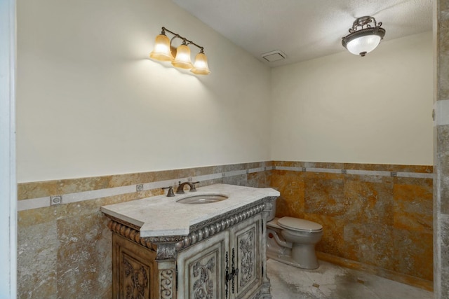 bathroom featuring vanity, tile patterned flooring, toilet, tile walls, and a textured ceiling