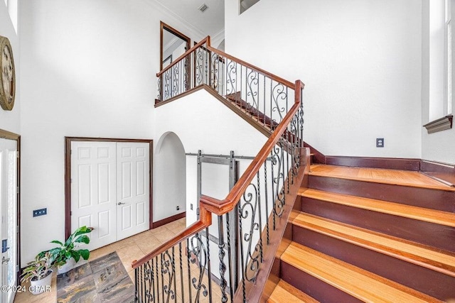 staircase with crown molding, a towering ceiling, and tile patterned floors