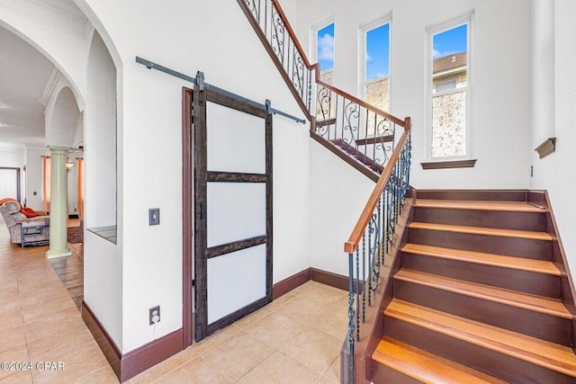 stairway featuring ornamental molding, tile patterned flooring, a barn door, and decorative columns