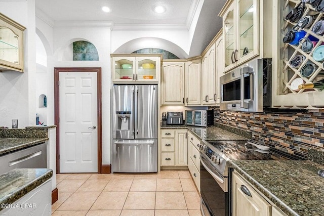 kitchen with light tile patterned flooring, dark stone countertops, ornamental molding, decorative backsplash, and appliances with stainless steel finishes