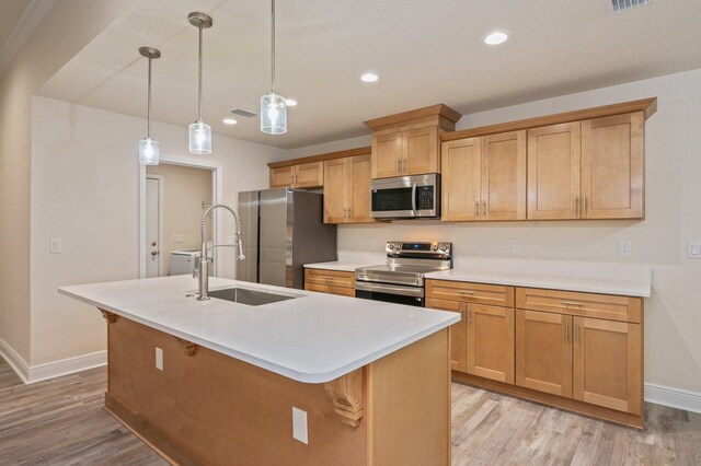 kitchen with sink, an island with sink, stainless steel appliances, and decorative light fixtures