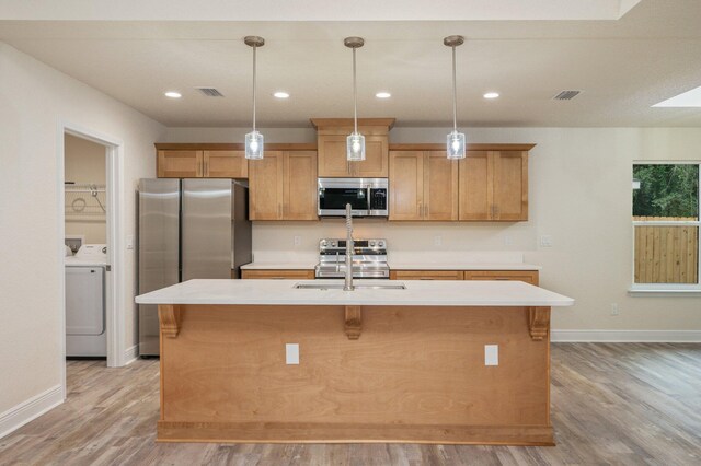 kitchen featuring a center island with sink, light wood-type flooring, stainless steel appliances, and washer / clothes dryer