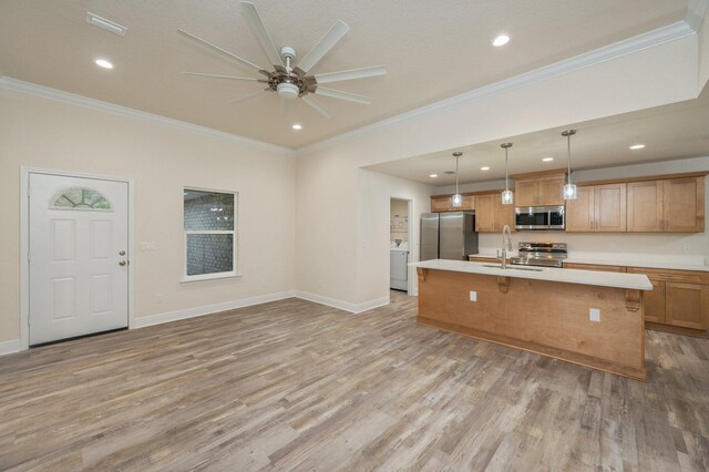 kitchen with stainless steel appliances, crown molding, decorative light fixtures, washer / dryer, and an island with sink