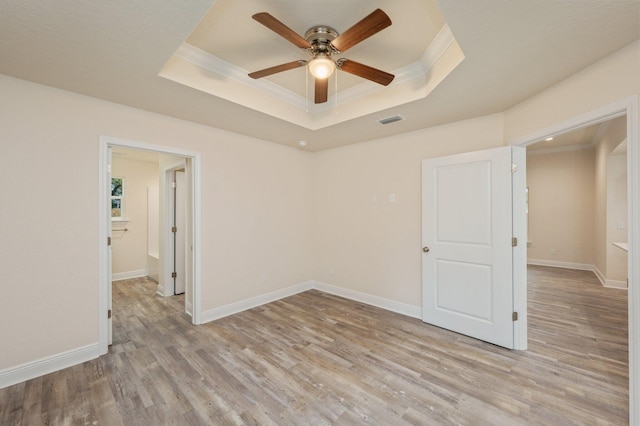 empty room with ceiling fan, a raised ceiling, ornamental molding, and light hardwood / wood-style flooring