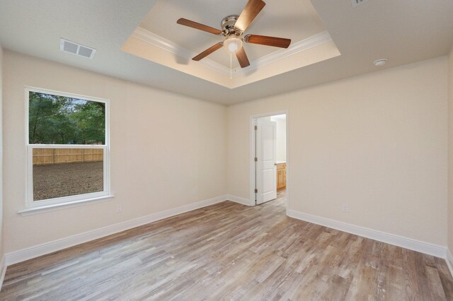 empty room featuring a raised ceiling, ceiling fan, light hardwood / wood-style flooring, and ornamental molding