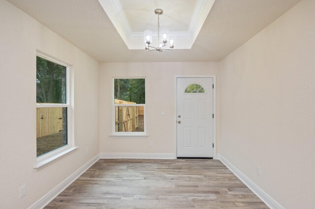 entryway with a raised ceiling, light wood-type flooring, ornamental molding, and an inviting chandelier