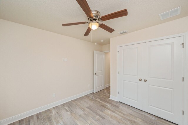 unfurnished bedroom with ceiling fan, a closet, a textured ceiling, and light hardwood / wood-style flooring