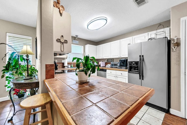 kitchen featuring a healthy amount of sunlight, stainless steel appliances, tile countertops, and white cabinetry