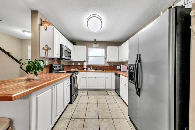 kitchen with white cabinets, tile countertops, light tile patterned floors, kitchen peninsula, and appliances with stainless steel finishes