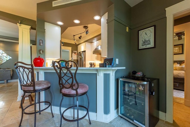 kitchen with a breakfast bar area, kitchen peninsula, stainless steel refrigerator, and white cabinets