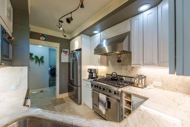 kitchen featuring white cabinets, appliances with stainless steel finishes, light stone counters, and wall chimney range hood