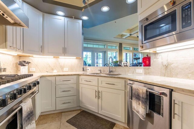 kitchen with light stone countertops, sink, stainless steel appliances, wall chimney range hood, and wine cooler