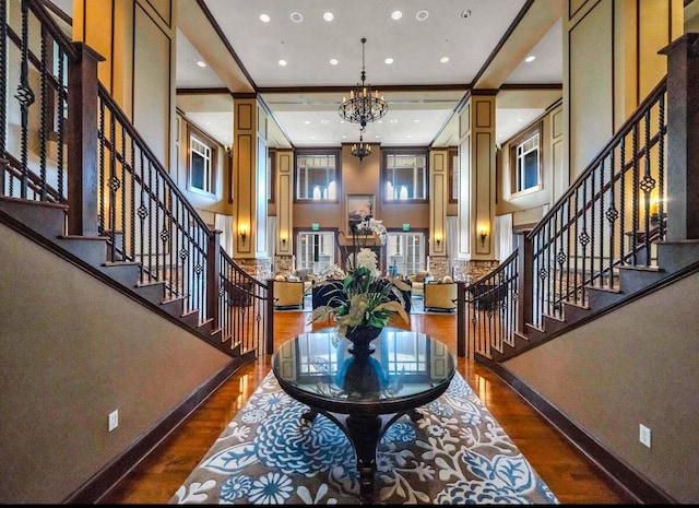 entryway featuring a towering ceiling, decorative columns, dark hardwood / wood-style flooring, a notable chandelier, and crown molding