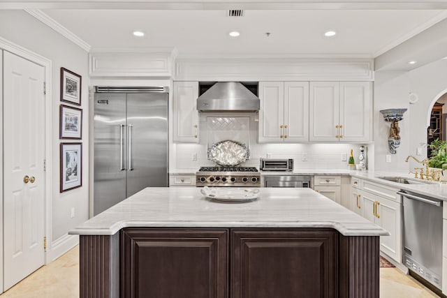 kitchen with sink, wall chimney range hood, appliances with stainless steel finishes, light stone counters, and a kitchen island