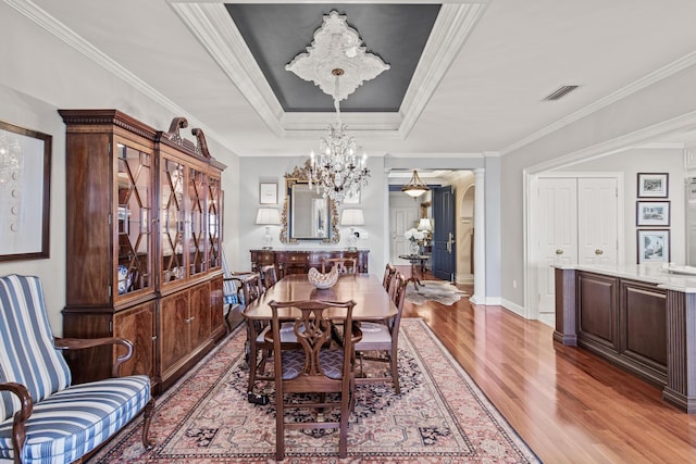 dining room with hardwood / wood-style floors, a tray ceiling, ornamental molding, a chandelier, and ornate columns