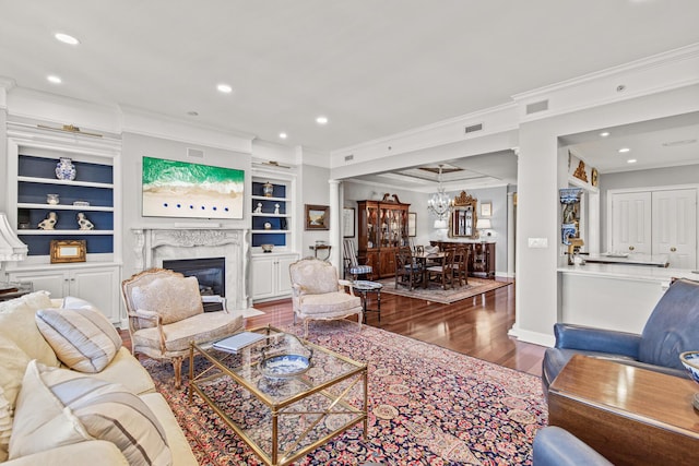 living room with built in features, hardwood / wood-style flooring, ornamental molding, a premium fireplace, and an inviting chandelier