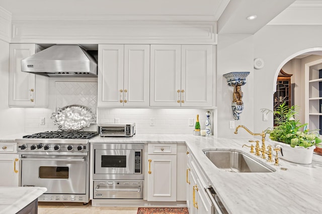 kitchen with appliances with stainless steel finishes, sink, white cabinets, light stone countertops, and wall chimney range hood