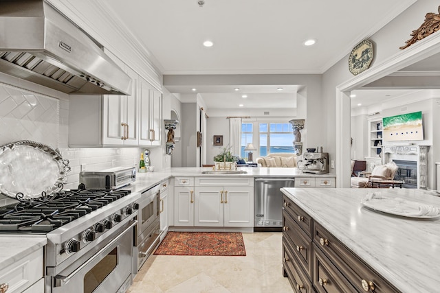 kitchen featuring sink, tasteful backsplash, stainless steel appliances, light stone countertops, and wall chimney range hood