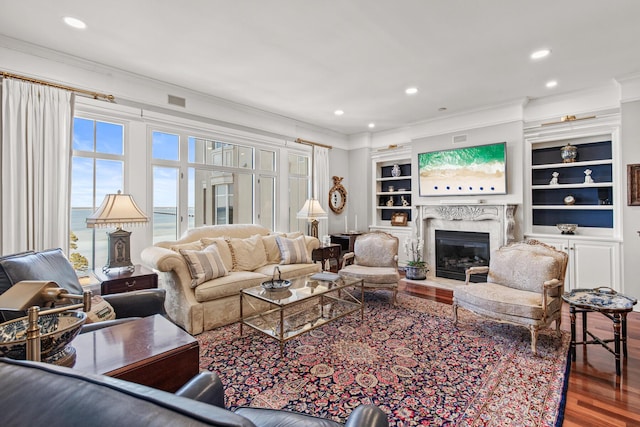 living room featuring hardwood / wood-style flooring, ornamental molding, built in features, and a fireplace