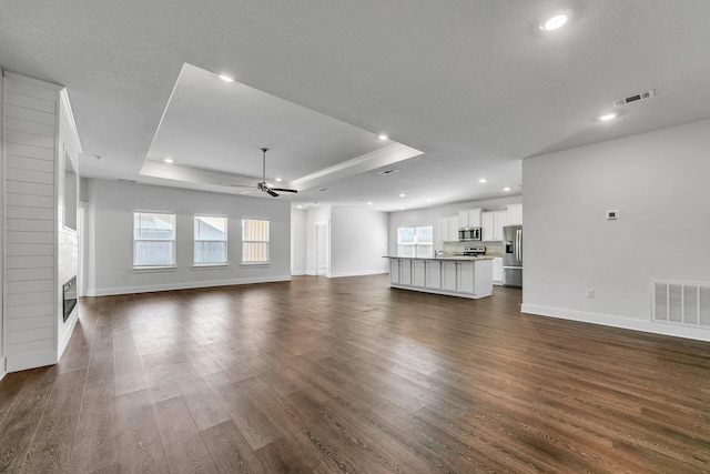 unfurnished living room with a fireplace, a textured ceiling, dark hardwood / wood-style floors, and a raised ceiling