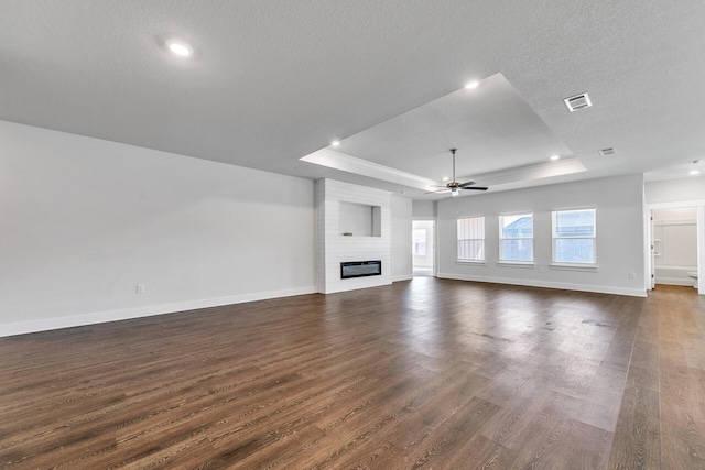 unfurnished living room featuring a textured ceiling, dark hardwood / wood-style floors, a raised ceiling, and a fireplace