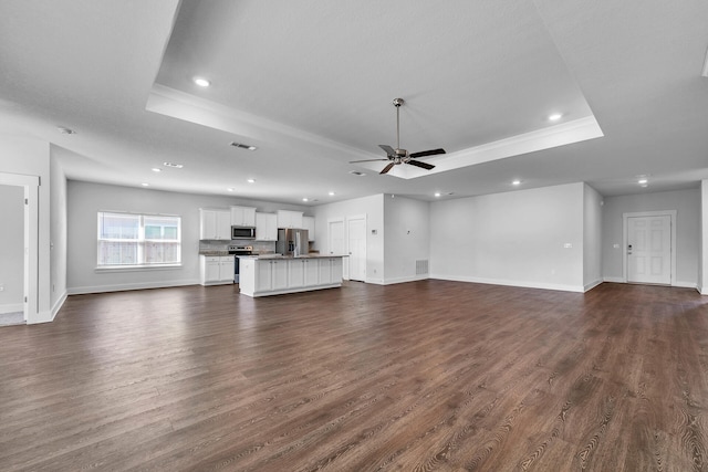 unfurnished living room featuring ceiling fan, dark hardwood / wood-style flooring, and a tray ceiling