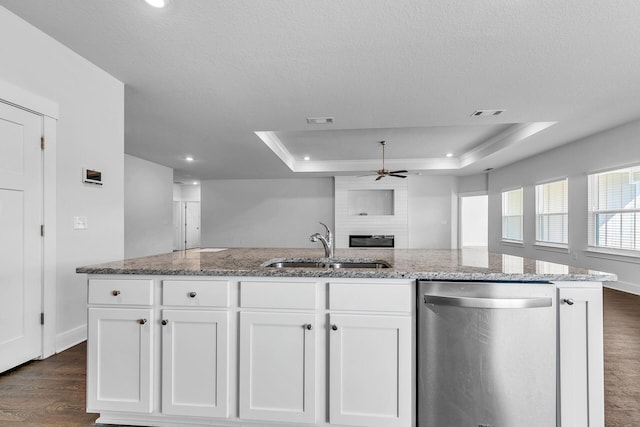 kitchen featuring stainless steel dishwasher, light stone countertops, a raised ceiling, and white cabinetry