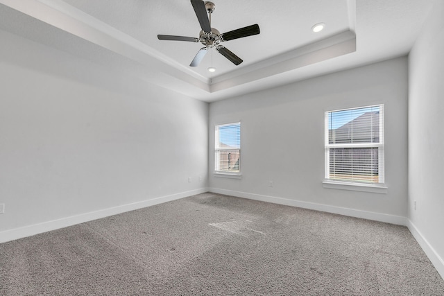 carpeted spare room with a raised ceiling and ceiling fan