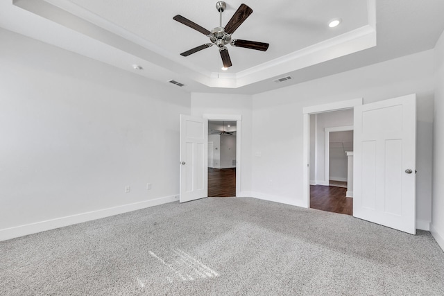 unfurnished bedroom with a closet, a walk in closet, a tray ceiling, and ceiling fan