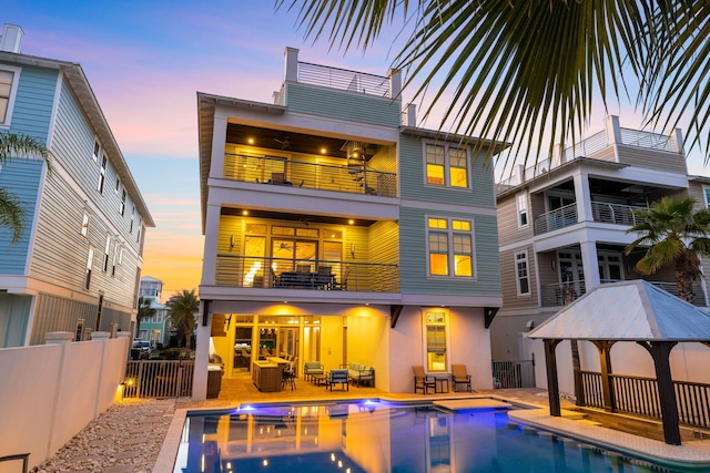 back house at dusk with outdoor lounge area, a patio, a balcony, a fenced in pool, and a gazebo