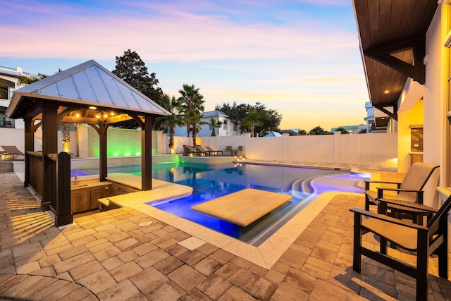 pool at dusk with a jacuzzi, a gazebo, and a patio area