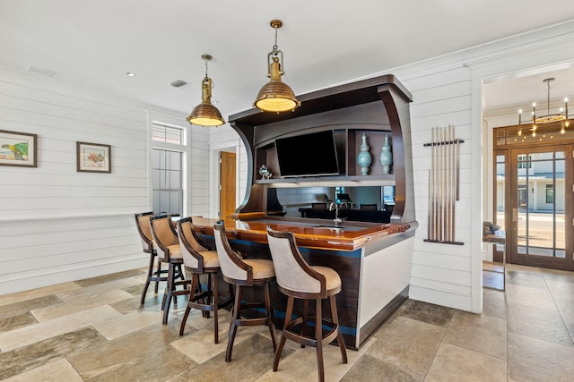 kitchen with a breakfast bar, plenty of natural light, hanging light fixtures, and wood walls