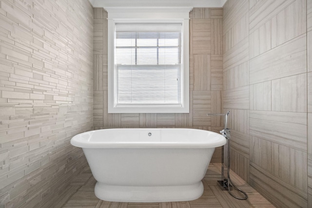 bathroom with a wealth of natural light, a bathtub, and tile walls