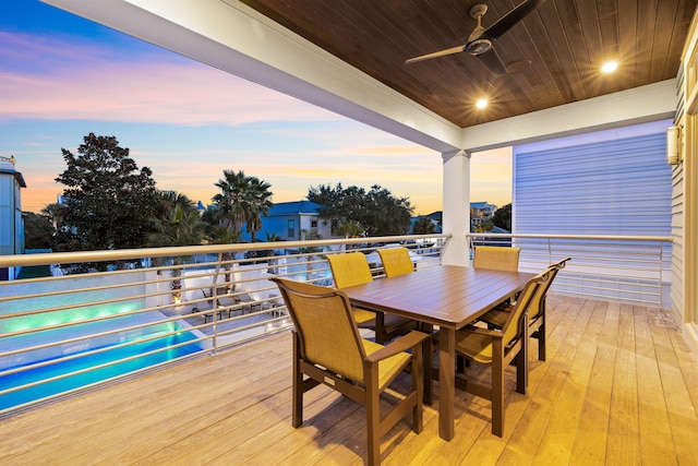 deck at dusk featuring ceiling fan and a pool