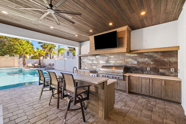 view of patio featuring ceiling fan, exterior kitchen, an outdoor wet bar, grilling area, and a fenced in pool