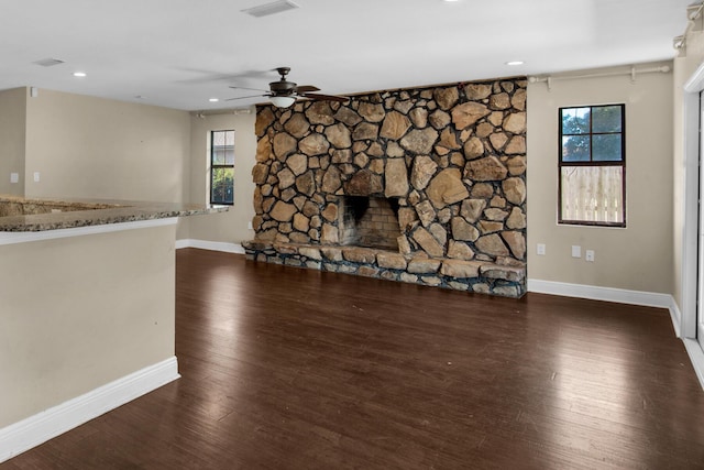 unfurnished living room featuring a stone fireplace, dark wood-type flooring, visible vents, and baseboards