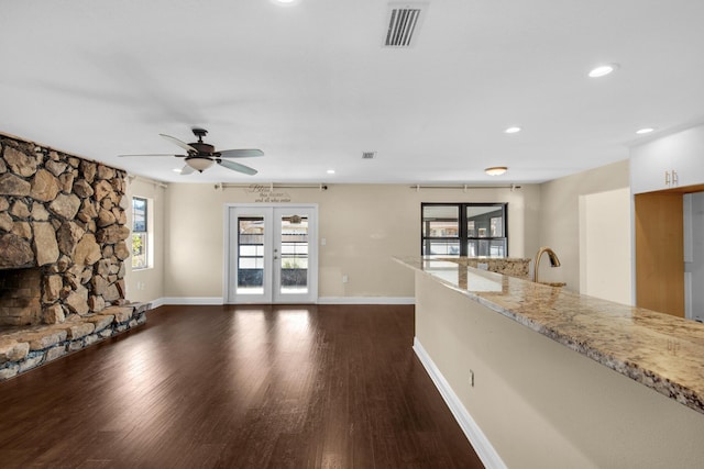 unfurnished living room with baseboards, visible vents, french doors, dark wood-style floors, and a stone fireplace