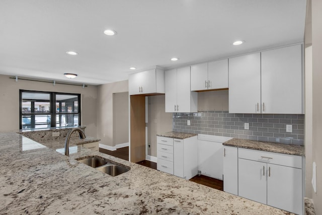 kitchen with white cabinets, a sink, backsplash, and light stone countertops